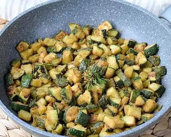 Zucchine gratinate in padella, dorate e saporite, con un rametto di rosmarino fresco.