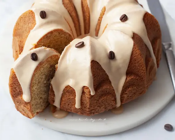 Deliziosa torta al caffè con glassa chiara e chicchi di caffè come decorazione. Una fetta è stata tagliata, mostrando la morbidezza dell'interno.