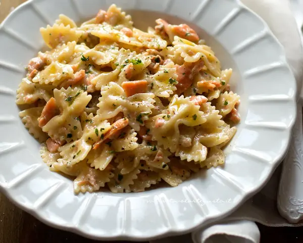 Farfalle cremose con pezzetti di salmone e prezzemolo tritato, un piatto invitante di pasta al salmone.
