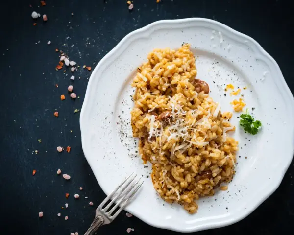 Un piatto di risotto funghi e salsiccia, guarnito con parmigiano grattugiato e prezzemolo, pronto per essere gustato.