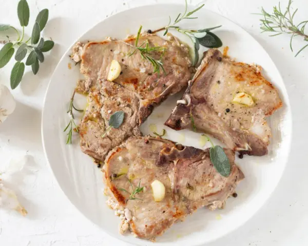 Tre succulente braciole di maiale cotte alla perfezione, guarnite con aglio, rosmarino e salvia.