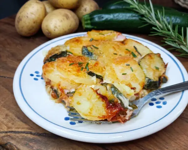 Piatto invitante di patate e zucchine al forno, dorate e filanti, con rosmarino fresco. Un contorno perfetto per ogni pasto.