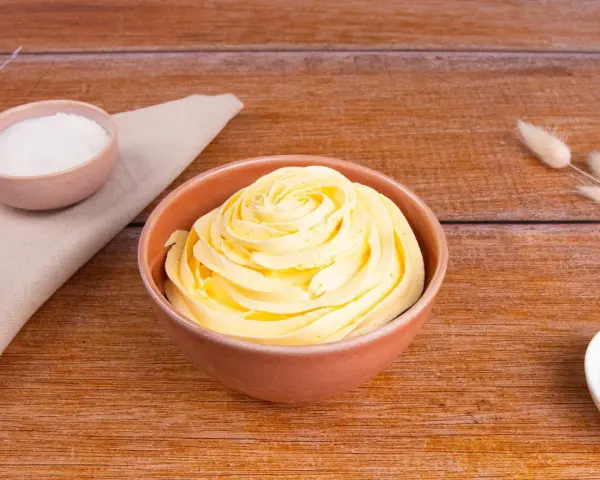 Una ciotola piena di soffice crema al burro, pronta per decorare torte. Accanto, ciotoline con zucchero e decorazioni naturali.