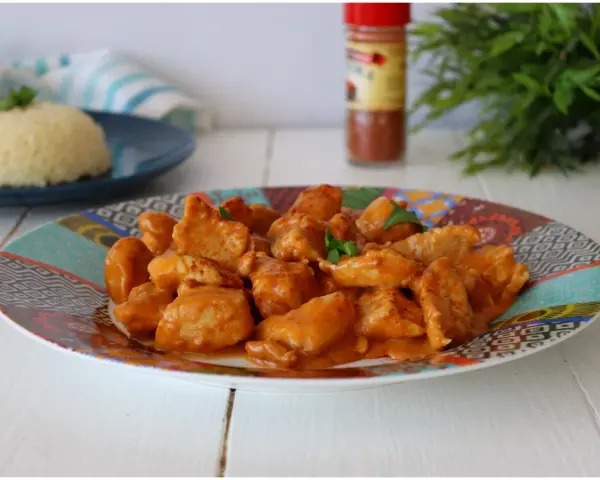 Succulento pollo alla paprika in una salsa cremosa, servito su un piatto colorato con riso bianco sullo sfondo.