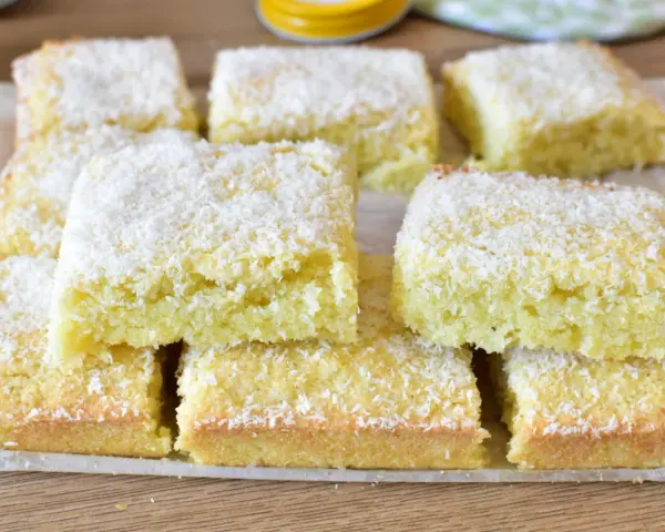 Fette di torta al cocco, soffici e dorate, cosparse di scaglie bianche. Un dolce profumato e invitante.