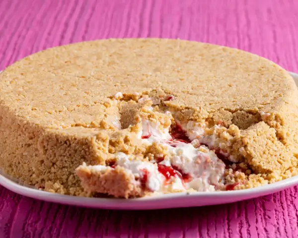 Cheesecake con yogurt greco e marmellata di fragole, con una crosta friabile di biscotti. Un morso goloso rivela il ripieno cremoso.
