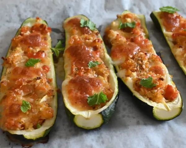Zucchine tonde ripiene al forno, dorate e filanti, guarnite con foglie di menta fresca.