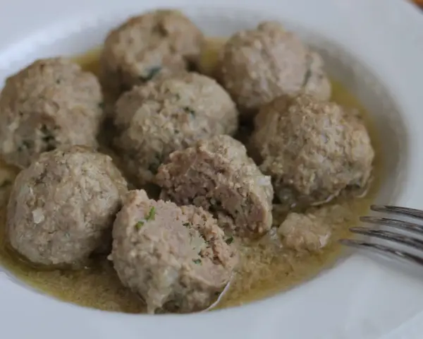 Polpette in umido, morbide e succulente, servite in un piatto bianco con un sughetto invitante.