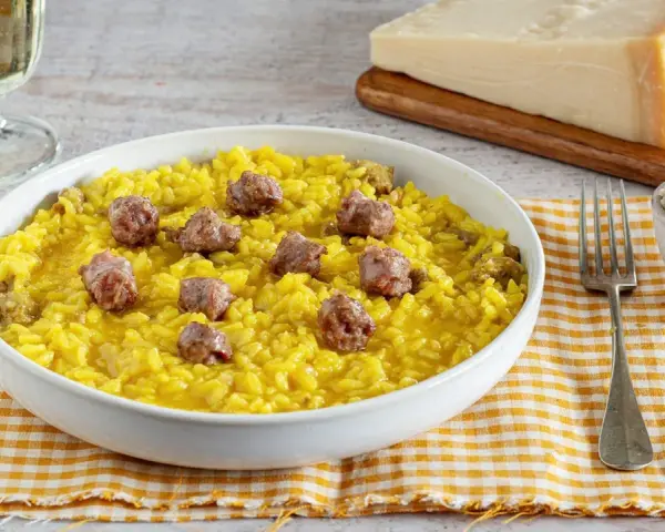 Un invitante risotto alla monzese, giallo intenso e arricchito da pezzetti di salsiccia, pronto per essere gustato.