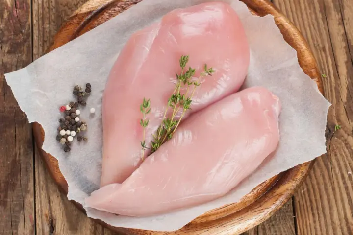 Due petti di pollo crudi, freschi e succulenti, adagiati su carta forno con pepe misto e rametti di timo.