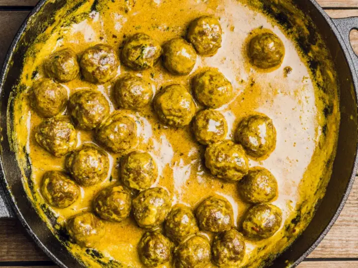 Polpette in bianco cremose in padella, dorate e succulente, immerse in una salsa gialla e invitante.
