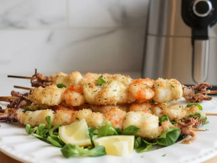 Spiedini di gamberi e calamari dorati e croccanti, cotti alla perfezione nella friggitrice ad aria. Serviti su un letto di insalata con spicchi di limone.