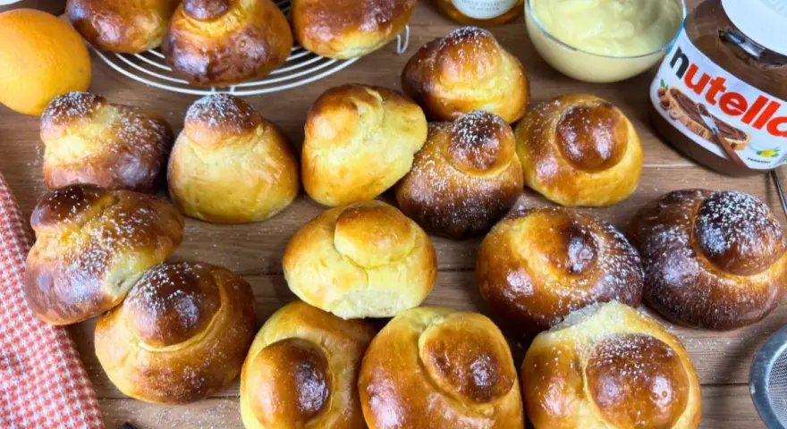 Tanti brioche col tuppo dorati, alcuni spolverati di zucchero a velo, pronti per essere farciti con crema o Nutella.