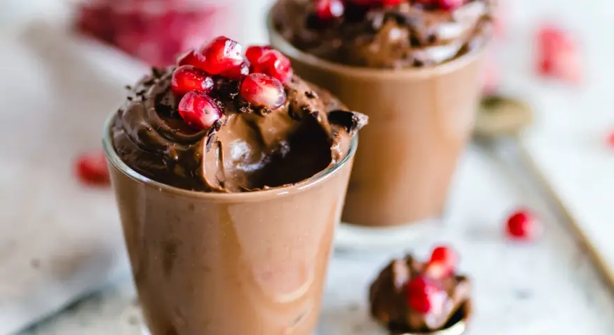 Due bicchierini di golosa mousse al cioccolato, guarniti con chicchi di melagrana e scaglie di cioccolato.