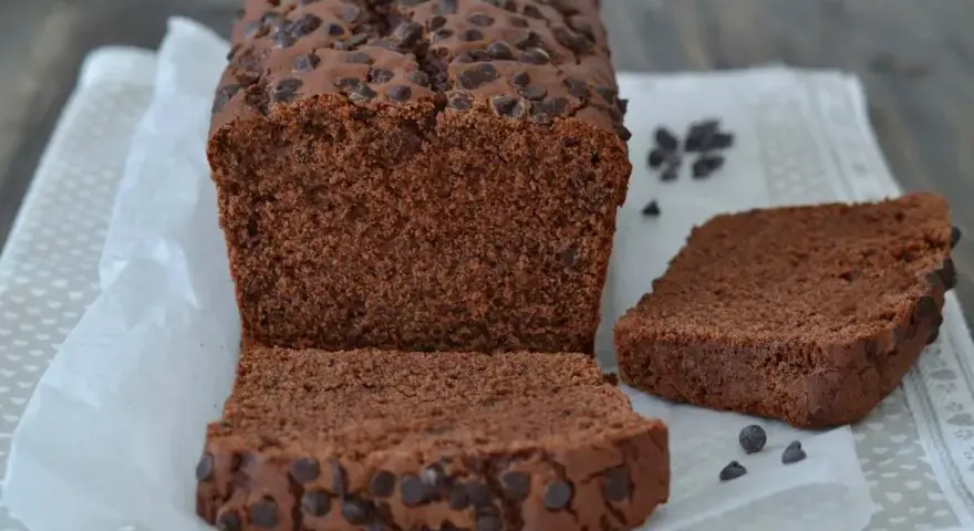 Un soffice plumcake al cioccolato, ricco di gocce, è tagliato a fette su carta da forno.