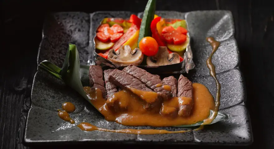 Straccetti di manzo succulenti su un piatto scuro, accompagnati da verdure miste e una salsa cremosa.