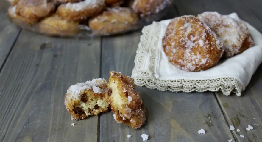 Frittelle di riso ricetta della nonna: dolcetti dorati e zuccherati, uno aperto rivela l'interno soffice e i chicchi d'uva passa.