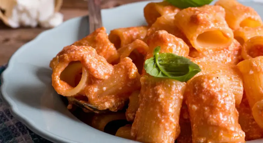 Piatto di pasta ricotta e pomodorini, condita con una cremosa salsa e guarnita con foglie di basilico fresco.