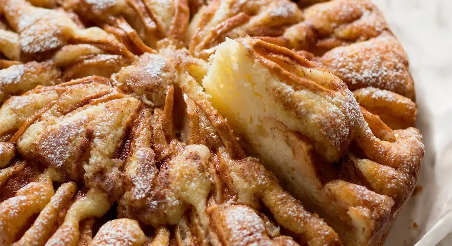 Una deliziosa torta di mele, cosparsa di zucchero a velo, con una fetta sollevata che rivela la morbida consistenza.
