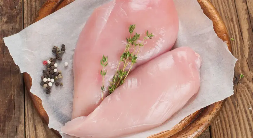 Due petti di pollo crudi, freschi e succulenti, adagiati su carta forno con pepe misto e rametti di timo.