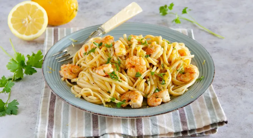 Un piatto di pasta con gamberetti, condita con limone e prezzemolo, accompagnata da limoni freschi e parmigiano.