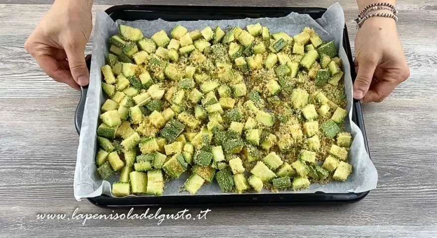 Zucchine gratinate al forno pronte per essere infornate, tagliate a cubetti e cosparse di pangrattato.