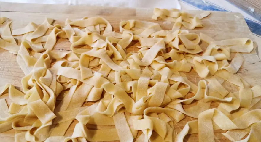 Fettuccine fresche, tagliatelle fatte in casa sparse su un tagliere di legno, pronte per essere cucinate.