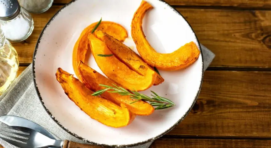 Fette di zucca al forno dorate e profumate, guarnite con rosmarino fresco, pronte per essere gustate.