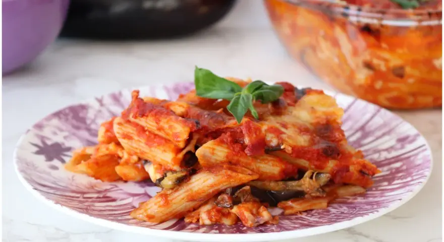 Piatto di pasta alla siciliana con melanzane, pomodoro e basilico, appena sfornata.