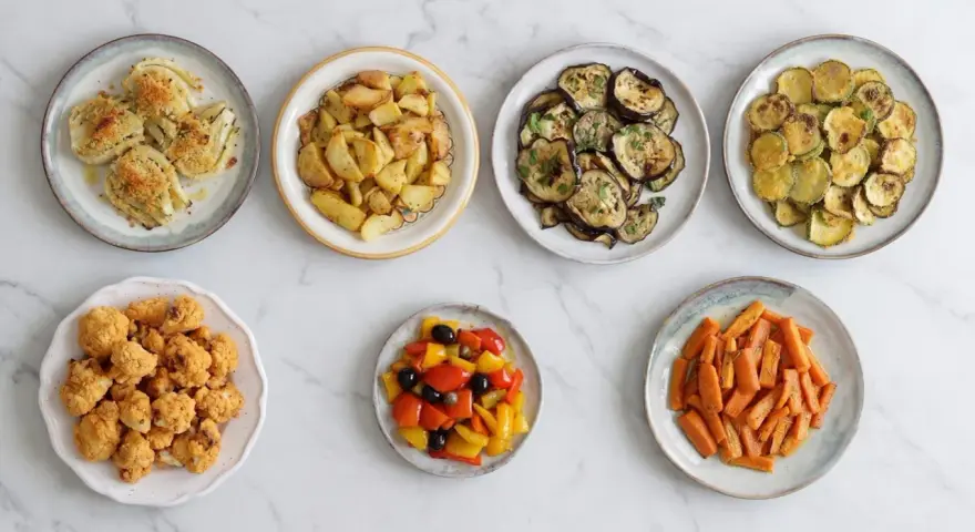 Sette piatti di verdure in friggitrice ad aria: finocchi gratinati, patate arrosto, melanzane, zucchine, cavolfiore fritto, peperoni e carote.