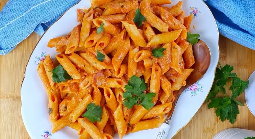 Piatto di penne al baffo cremose, guarnite con prezzemolo fresco, pronte per essere gustate.