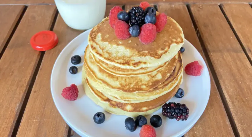 Pila di pancake senza zucchero guarnita con frutti di bosco freschi, accompagnata da un bicchiere di latte.