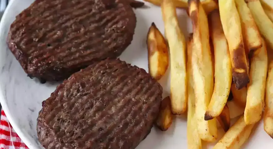 Due hamburger in friggitrice ad aria con patatine fritte dorate su un piatto bianco.