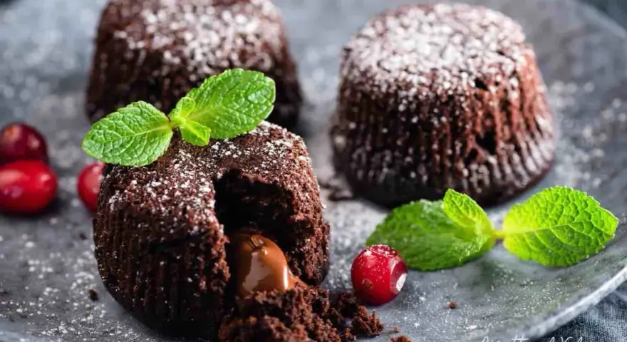 Tre tortini al cioccolato con cuore fondente, guarniti con menta e frutti rossi, spolverati di zucchero a velo.