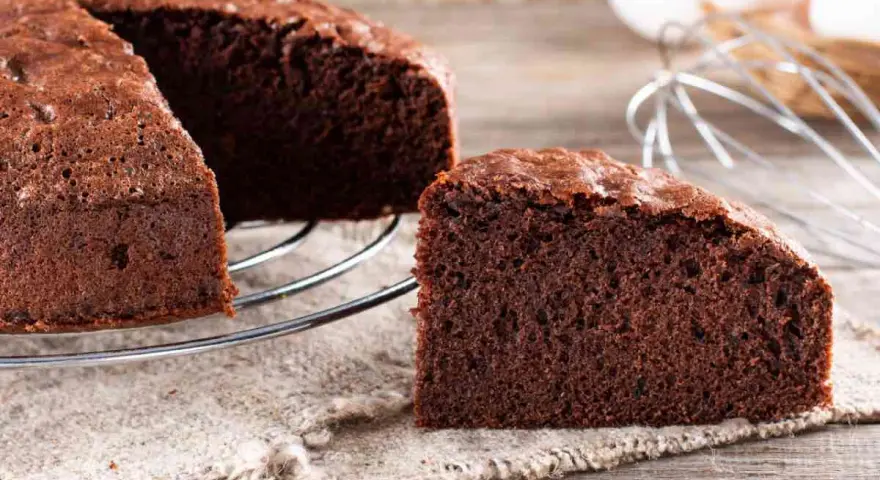 Una fetta di torta al cioccolato soffice e invitante, appena sfornata, su un tavolo di legno.
