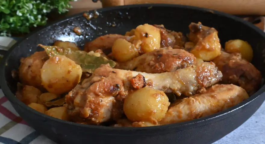 Un saporito pollo in umido con patate e alloro, cotto in una padella di ghisa, pronto per essere gustato.