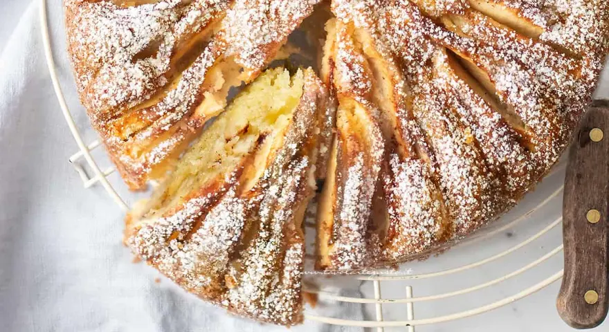 Deliziosa torta di mele in friggitrice ad aria, spolverata di zucchero a velo, con una fetta tagliata per mostrare il morbido interno.