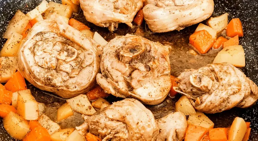Porzioni di ossobuco di tacchino cotte in padella con patate e carote a cubetti, condite con erbe aromatiche.