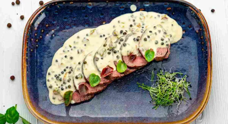 Fette fettine di filetto al pepe verde, ricoperte da una cremosa salsa, guarnite con germogli freschi e foglie verdi.