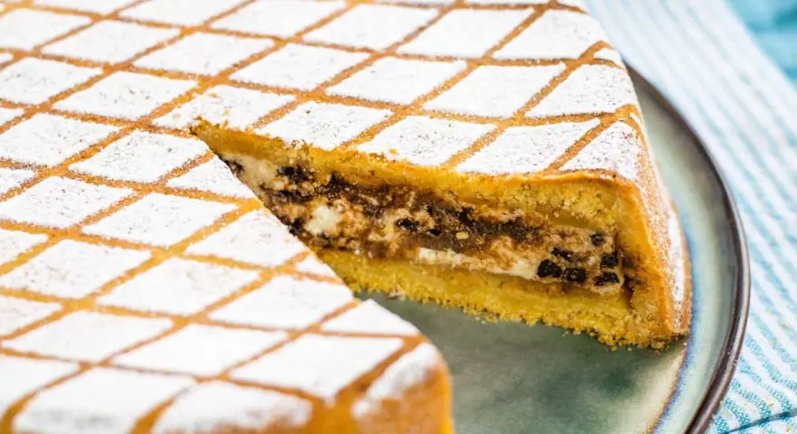 Una fetta di cassata al forno, con la sua copertura a rombi di zucchero a velo, rivela un ripieno goloso di ricotta e cioccolato.