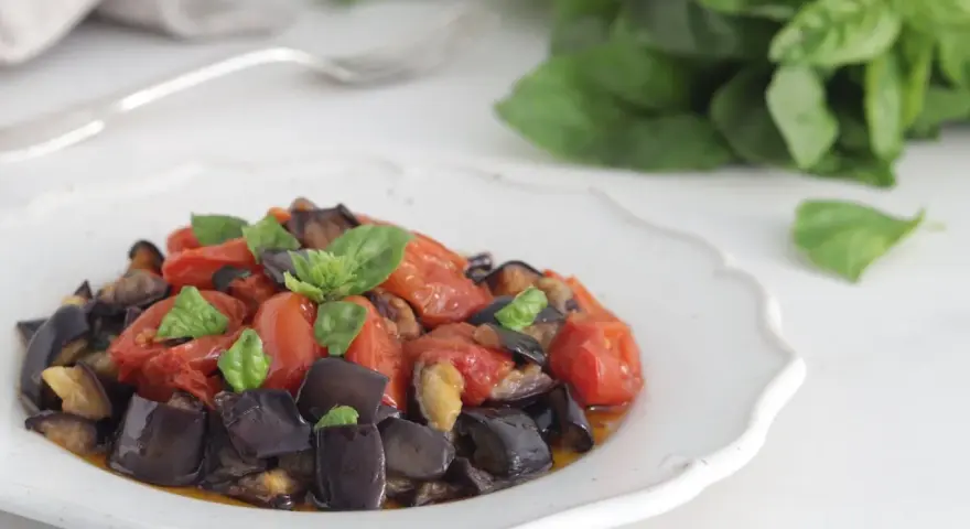 Un piatto invitante di melanzane a funghetto con pomodorini e basilico fresco, pronto per essere gustato.