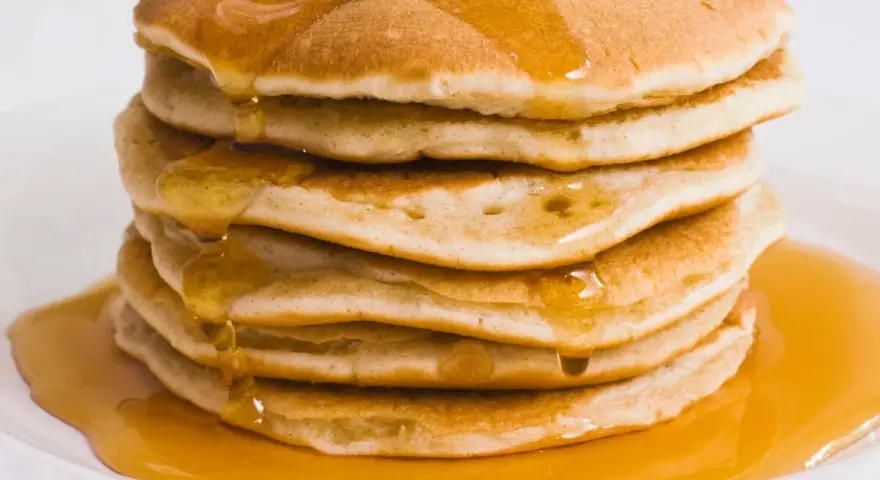 Pila di pancake dorati, inzuppati di sciroppo d'acero. Perfetti per una ricetta pancake proteici sana e golosa.