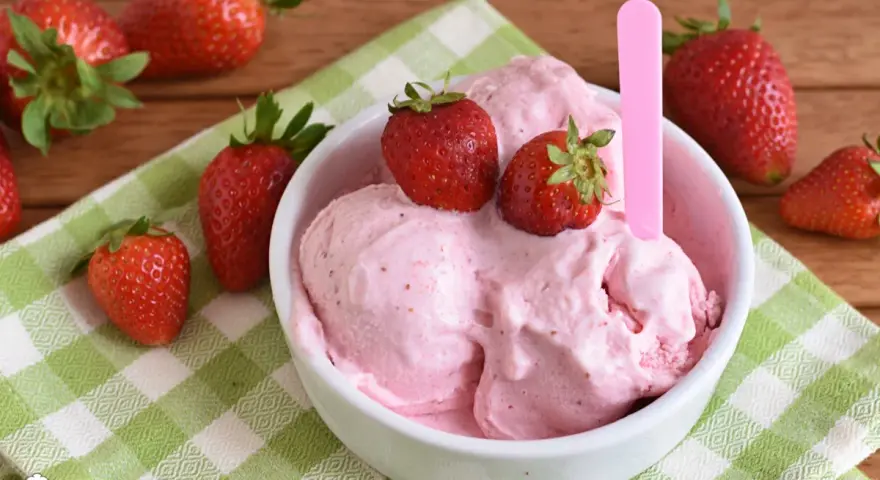Una ciotola di cremoso gelato alla fragola, guarnito con fragole fresche, su una tovaglietta a quadri verdi.