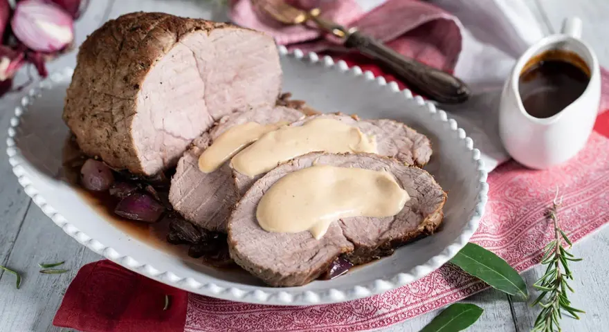 Arrosto di vitello morbido con sughetto benedetta, servito su un piatto bianco con cipolle rosse e rosmarino.