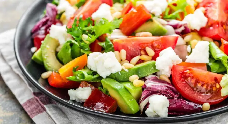 Insalata fresca con pomodori, lattuga, formaggio e avocado a fette, guarnita con pinoli.