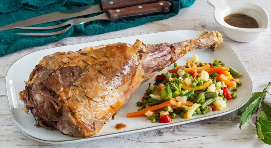 Succulento agnello al forno, dorato e profumato, servito con un contorno di verdure miste colorate.
