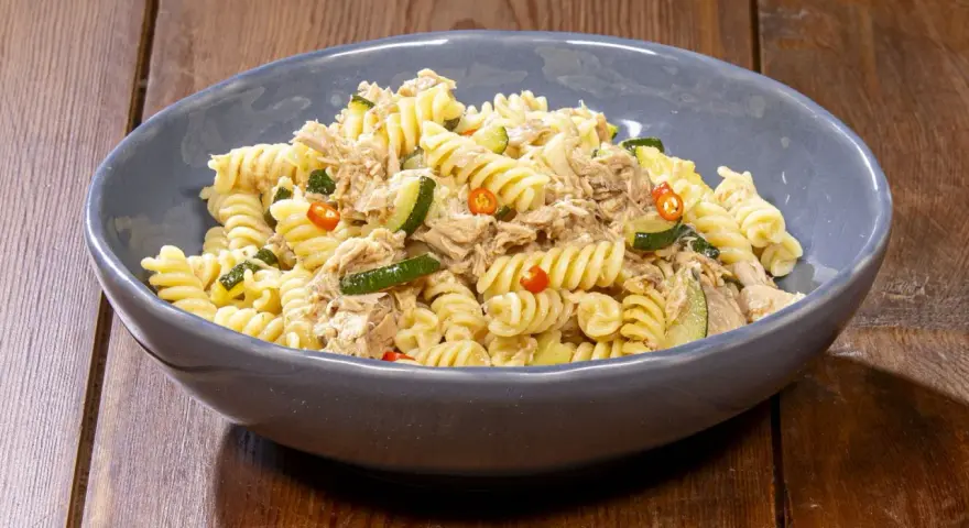 Fusilli con zucchine, tonno e peperoncino in una ciotola blu su un tavolo di legno. Un piatto semplice e gustoso.