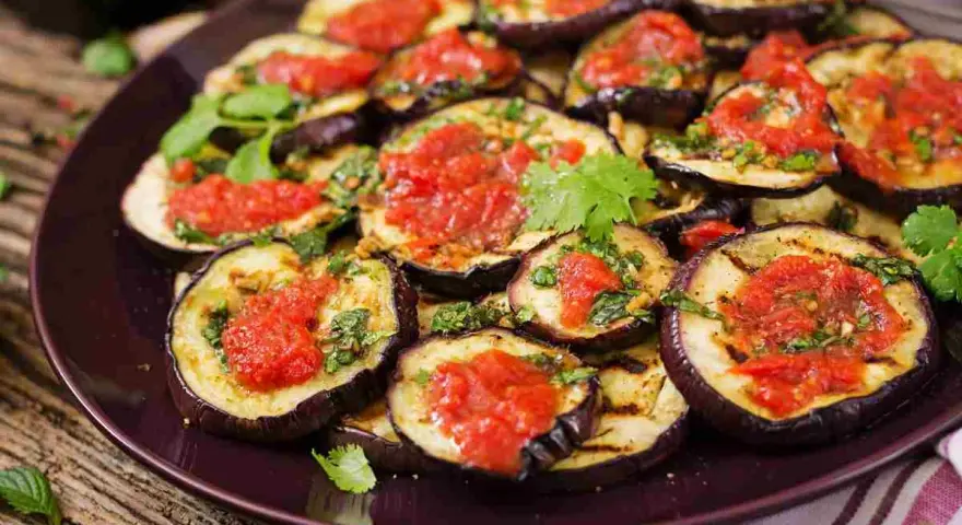 Fette di melanzane grigliate condite con salsa di pomodoro e basilico, un piatto invitante di melanzane alla pizzaiola.
