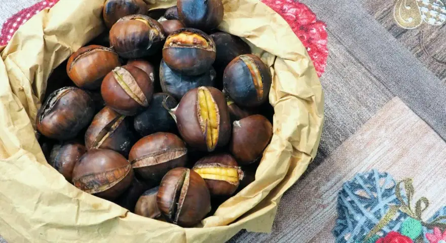 Castagne in friggitrice ad aria, pronte per essere gustate. Un sacchetto di carta marrone trabocca di castagne calde e dorate, alcune con tagli che rivelano il loro interno morbido.