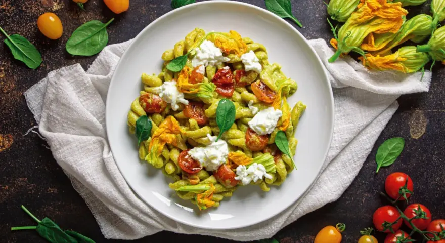 Piatto di pasta con crema di zucchine, pomodorini confit, fiori di zucca e ricotta fresca. Un tripudio di sapori estivi.